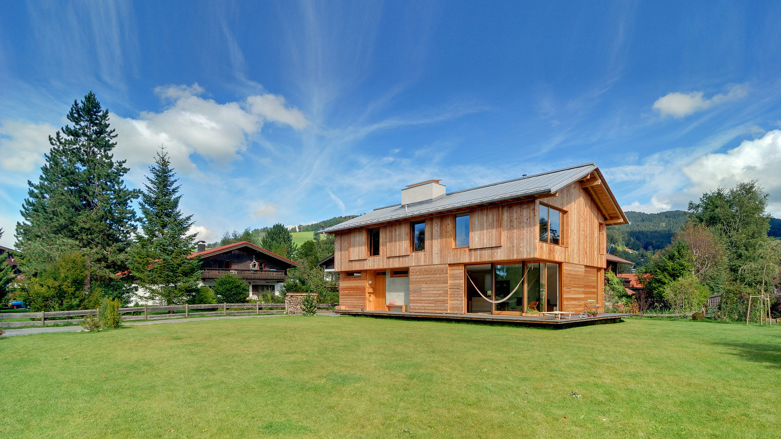 Rauchkuchlhaus – Das Rauchkuchlhaus ist ein grosszügig gebautes Einfamilienhaus mit einer Wohnfläche von fast 230 Quadratmetern. Es befindet sich auf einem Grundstück in Seenähe und ist von einem Holzdeck umgeben. Ein einziger Raum, angelehnt an Rauchkuchln, bei denen es sich um ursprüngliche Feuer- und Kochstellen mit grossen Kaminen handelt, bildet das Herzstück des Holzhauses. In zwei Steinen aus Sichtbeton sind die haustechnischen Funktionen untergebracht.