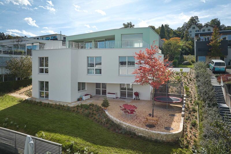 An der hangseitigen Fassade erweitern grosse, einladende Terrassen den Wohnraum ins Freie. Ob draussen oder drinnen – überall ist das Farbkonzept erkennbar, das Mint- und helle Crème- und Beigetöne vortrefflich vereint.