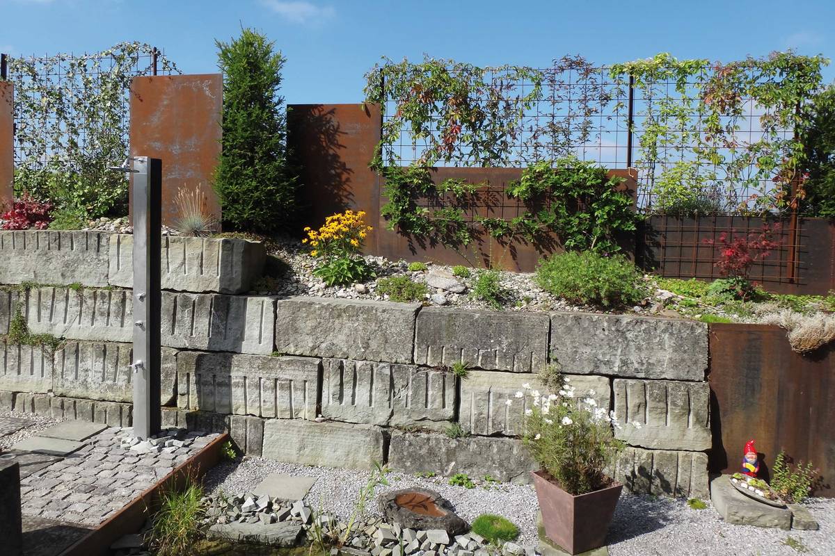 Eisenplatten, kombiniert mit rostigen Rankgittern, ergeben ein lockeres, spannungsvolles Gesamtbild. Abderhalden Gartenbau AG.