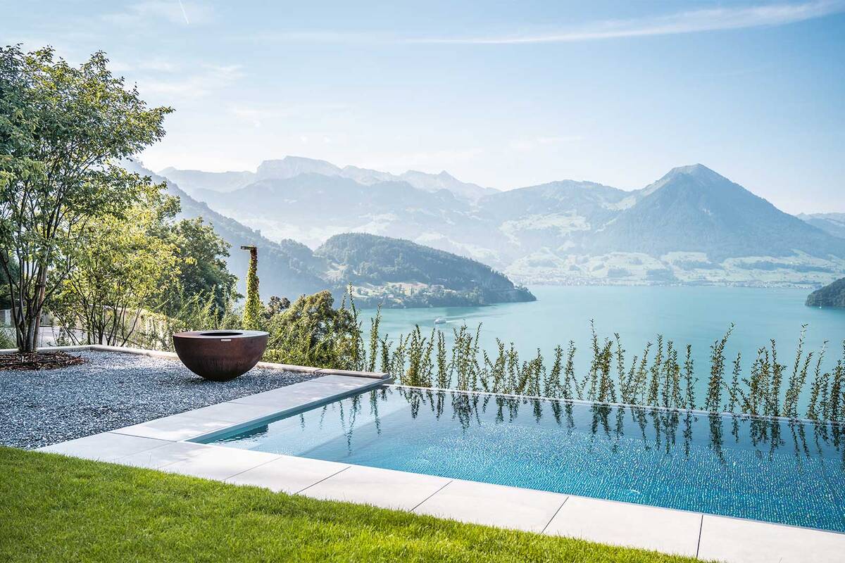 Zusammen mit der gekiesten Ruhezone im Schatten der Bäume und einer Feuerschale entsteht eine perfekte Outdoor-Wellness-Oase, um seine Batterien wieder aufzuladen. Edelstahlpool mit Infinity-Überlauf, LED-Unterwasserbeleuchtung und Jet-Düsen. Zireg Ziswiler GmbH.