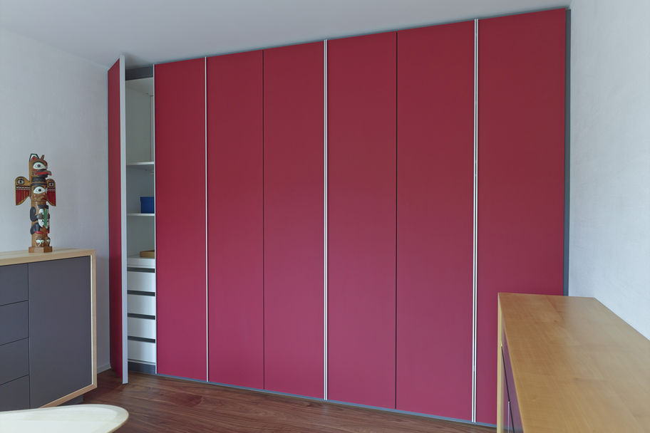 Mut zur Farbe: Der geräumige Schlafzimmerschrank bietet Platz für die gesamte Garderobe. Quadratische Tiefenfräsungen in der Wunschfarbe und die abgesetzten Griffprofile aus Aluminium lockern die lange Front optisch auf. Im Büro und Arbeitszimmer stehen Einbauschränke mit Fronten aus satiniertem Glas. Das Griffprofil erstreckt sich über die ganze Türhöhe.
