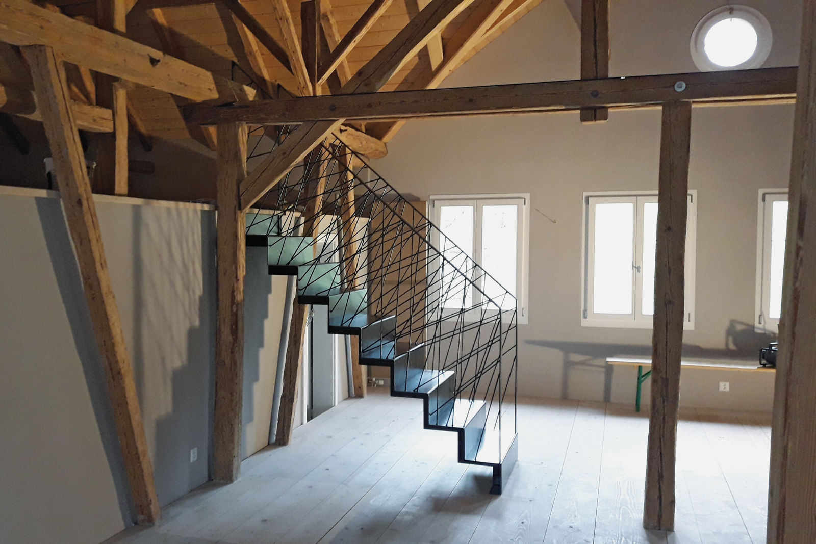 Die markante Faltwerktreppe aus Schwarzstahl mit dem filigranen Staketengeländer harmoniert gut mit den Balken des alten Bauernhauses.